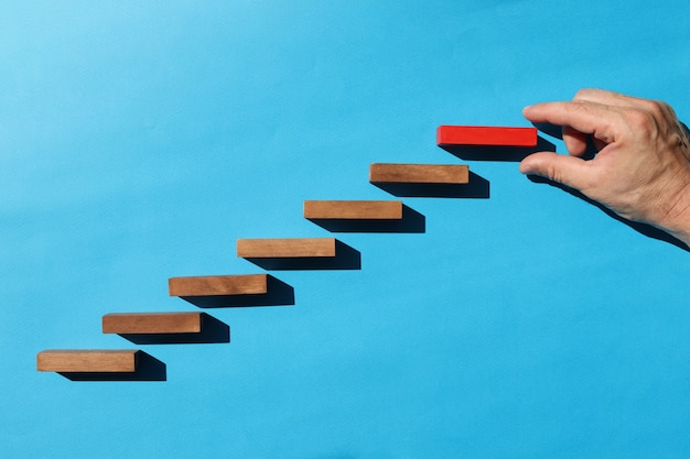 Male hand holding top red wooden block on blue background career growth goal achievement