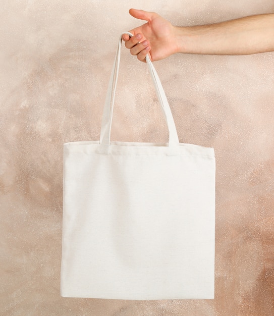 Male hand holding tote bag against brown background