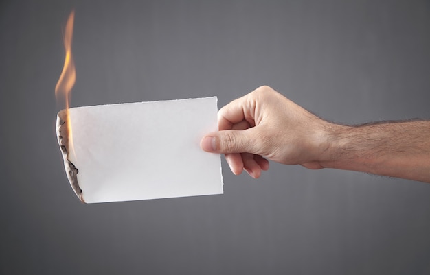 Male hand holding white burned paper.