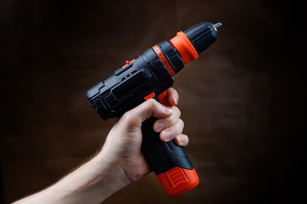 Male hand holds an electric screwdriver on a dark brown background.