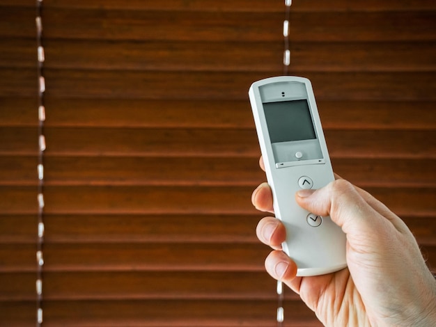 male hand holds a remote control to open the window blinds