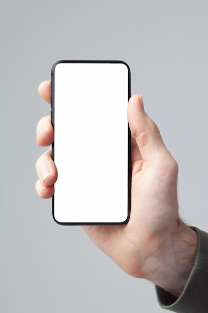 Male hand holds smratphone with white blank screen isolated on gray background