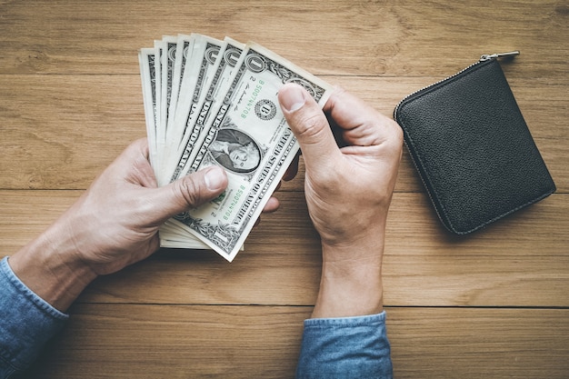 Male hand holing money dollar bill with wallet on wood table