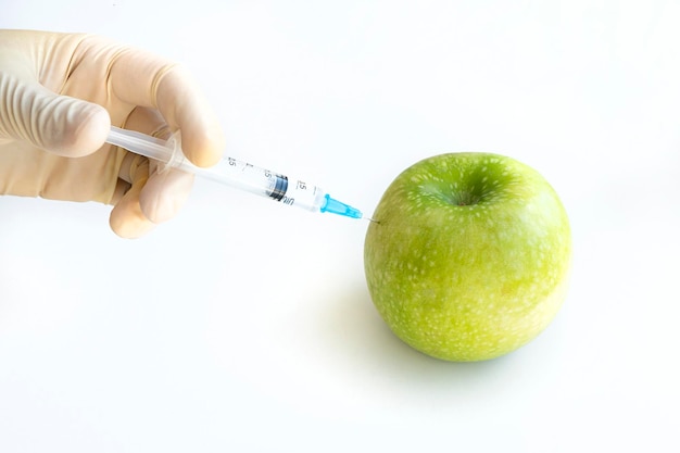 Male hand makes injection syringe into an apple isolated on white Laboratory research and fruit selection Genetically modified products concept