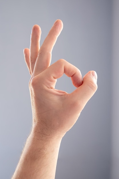 Male hand makes a sign ok on a gray background. Fingers show okay