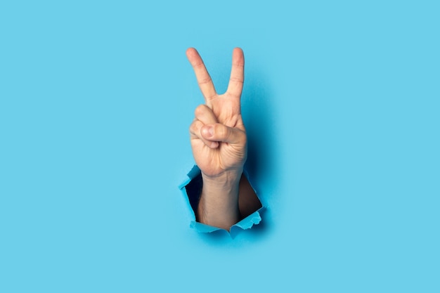 Male hand makes a two fingers up greeting gesture on blue