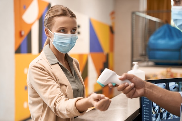 Male hand measuring body temperature of a young businesswoman wearing medical mask or female office