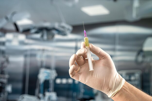 Male hand in protective gloves holding a plastic syring with liquid for injection preparing for surgery in the surgical office at the hospital