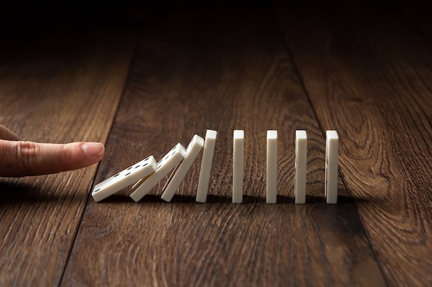 Male hand pushing white dominoes on a brown wood