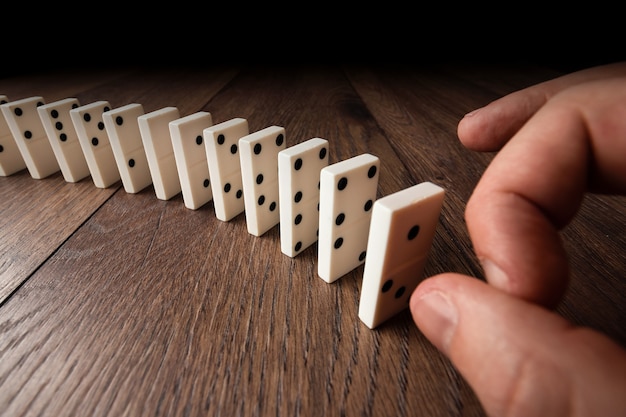 Male hand pushing white dominoes on brown wood