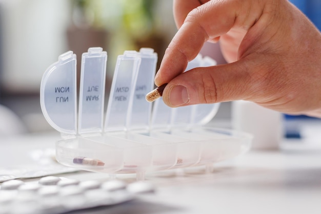 Male hand putting pills into open pill organizer or plastic pillbox