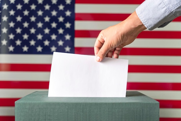 Male hand putting voting ballot into box on American flag background