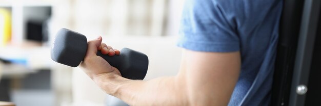 Male hand raising black dumbbell at home closeup