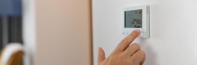 Male hand sets a programmable thermostat for heating and cooling closeup device controls the