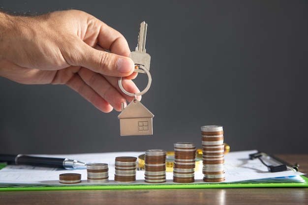 Male hand showing house keys over stack of coins