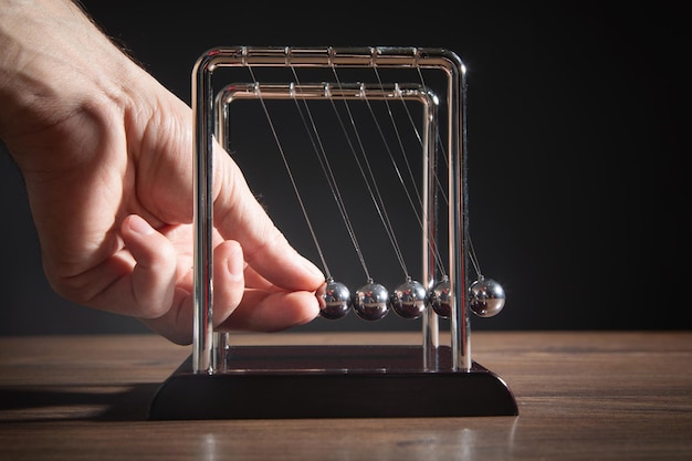 Male hand showing Newton's cradle balls on the wooden table Business