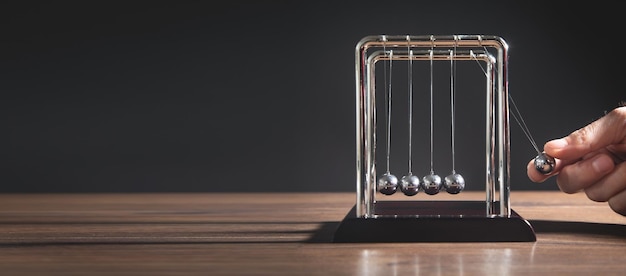 Male hand showing Newtons cradle balls on the wooden table Business