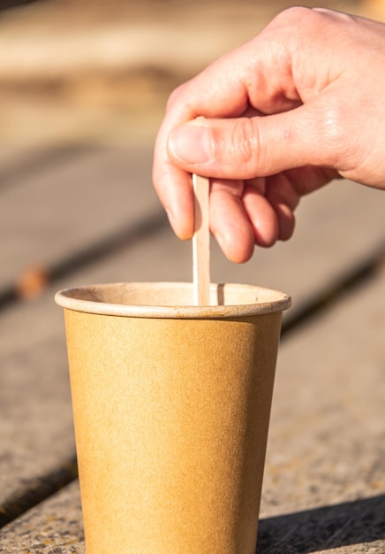 Male hand stirring a stick on a brown paper cup on a wooden surface