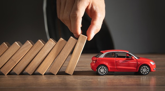 Male hand stopping wooden blocks from falling on red toy car