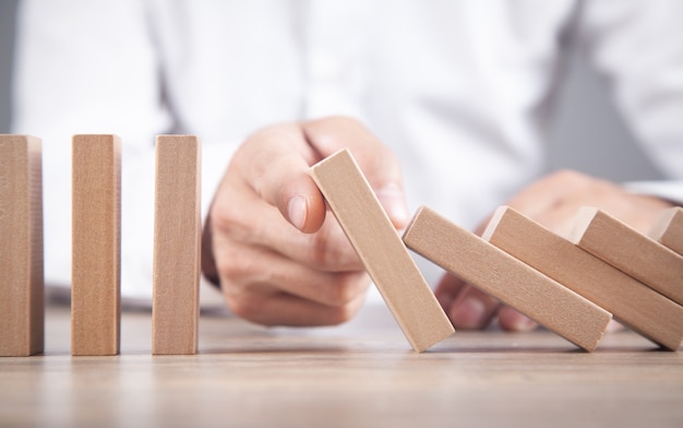 Male hand stopping wooden domino. Business. Crisis. Risk