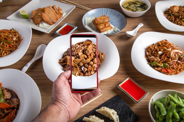 Male hand takes a photo with smartphone of the food on the table in the oriental restaurant.