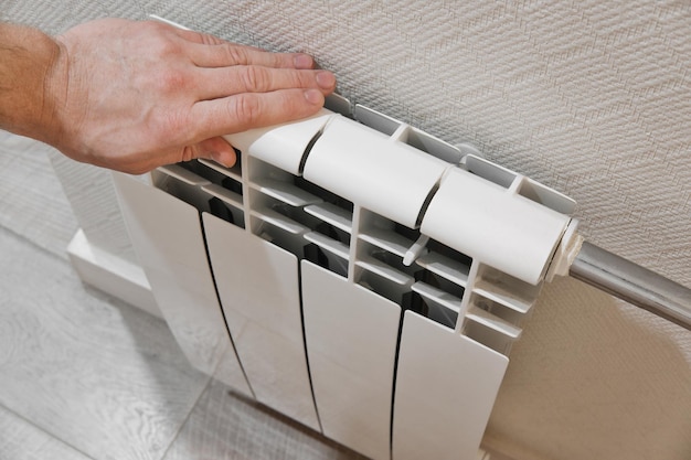 Male hand touching white home heating radiator Modern house heating technology