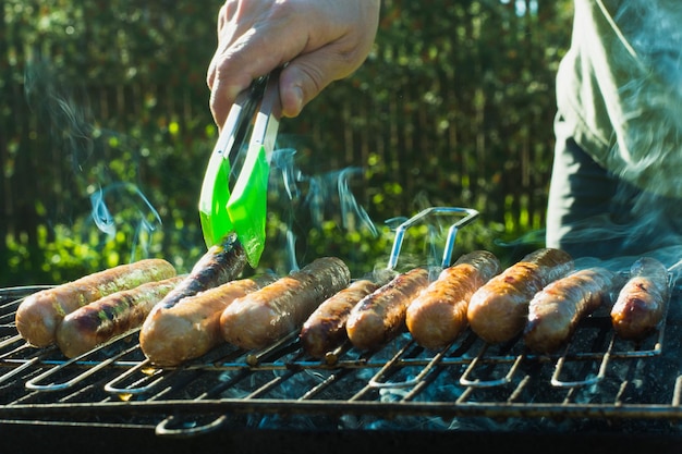 Male hand turned the sausages over an open fire barbecue Close up Outdoor