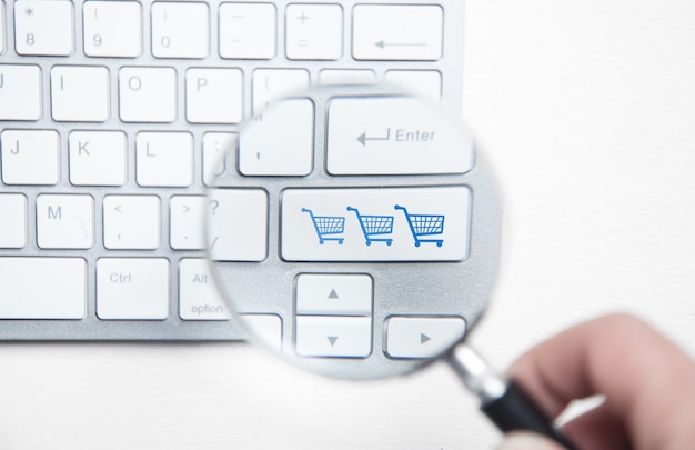 Male hand using magnifying glass. Shopping carts on computer keyboard. Online shopping