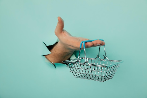 Male hand with shoppind basket on a blue paper background Sales concept