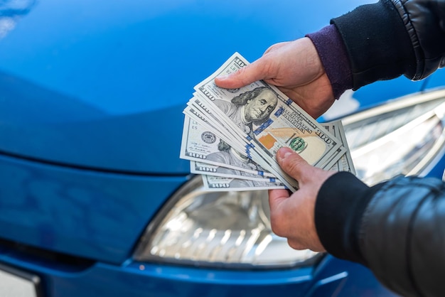 Male hands in a business suit hold dollars on a background of blue beautiful car