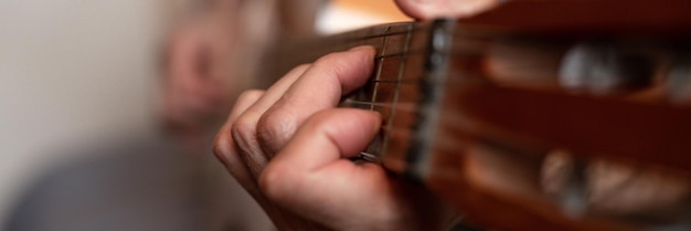 Male hands of an elderly senior caucasian man holding and playing a classical guitar close up at home unprofessional faceless guitarist people play amateur music domestic hobbies and leisure banner