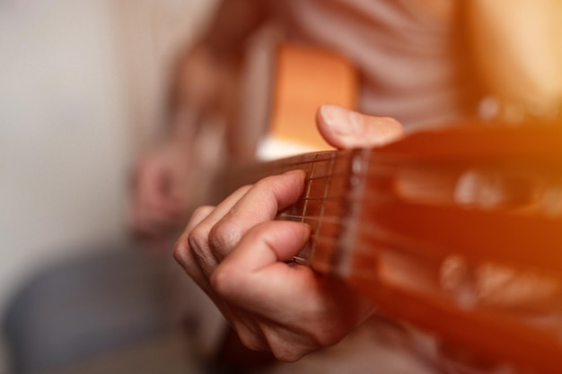 Male hands of an elderly senior caucasian man holding and playing a classical guitar close up at home unprofessional faceless guitarist people play amateur music domestic hobbies and leisure flare