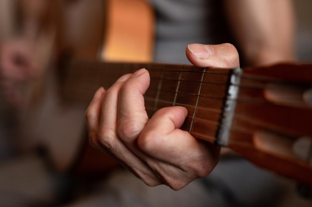 Male hands of an elderly senior caucasian man holding and playing a classical guitar close up at home unprofessional faceless guitarist people play amateur music domestic hobbies and leisure