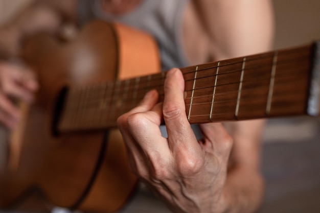 Male hands of an elderly senior caucasian man holding and playing a classical guitar close up at home unprofessional faceless guitarist people play amateur music domestic hobbies and leisure