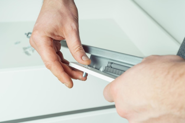 Male hands hold and insert metal screw to fix rail assembling drawer of white dresser or wardrobe