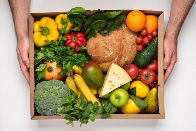 Male hands holding cardboard box full of fresh grocery products