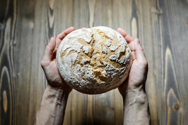 Male hands holding fresh baked bread loaf over wood background