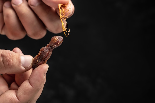 Male hands holding Tamarinds set beans in shell on a brown butchers block on a dark background Tropical healthy fruits banner menu recipe place for text