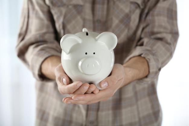 Male hands holding white piggy bank on blurred curtains background