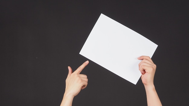 Male hands is holding and point finger to the A4 paper on black background.