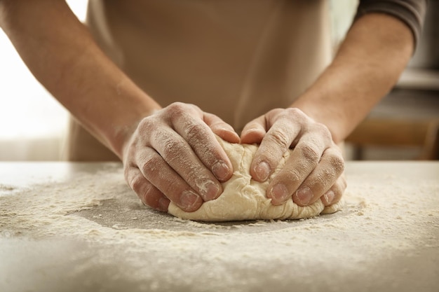 Male hands kneading dough on sprinkled with flour table closeup