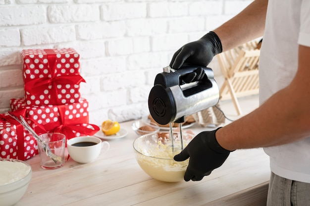 Male hands mixing dough with electric mixer in a kitchen closeup