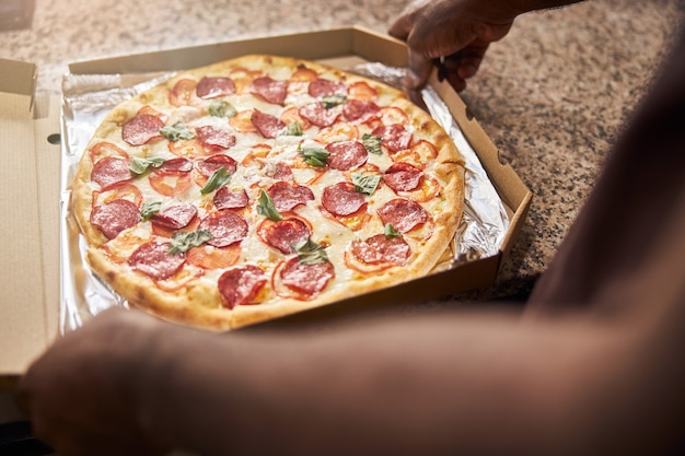 male hands packing delicious pepperoni pizza in delivery box