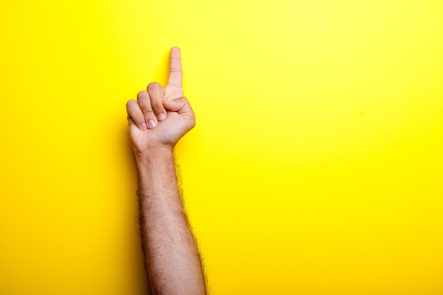 Male hands points up on yellow background. Studio photo