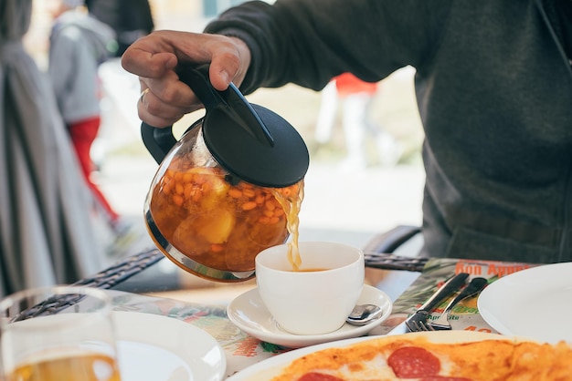 Male hands pouring with sea buckthorn tea in white cup