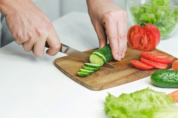 Male hands prepairing salad. Cutting cucumber .