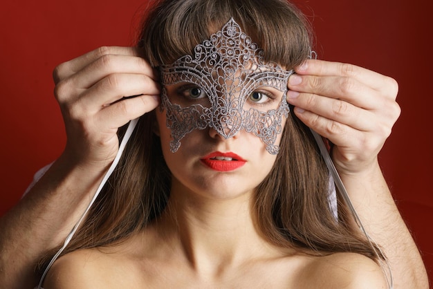 Male hands put lace mask on face beautiful girl with red lipstick on red