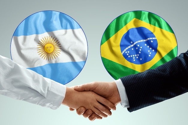 Male hands shaking hands against the background of the flags of Argentina and Brazil.