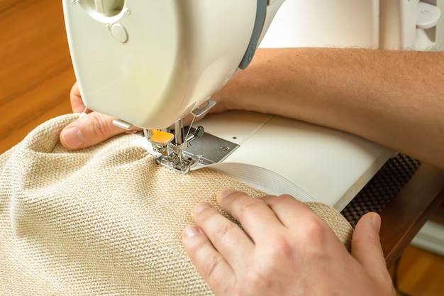 Male hands stitching white fabric on modern sewing machine Close up view of sewing process