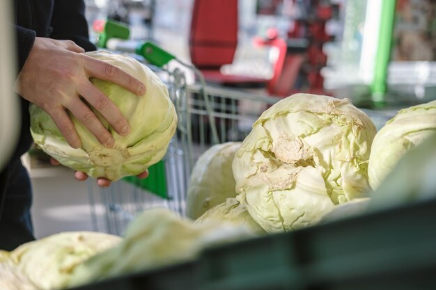 Male hands take fresh cabbage from the counter with vegetables in the store